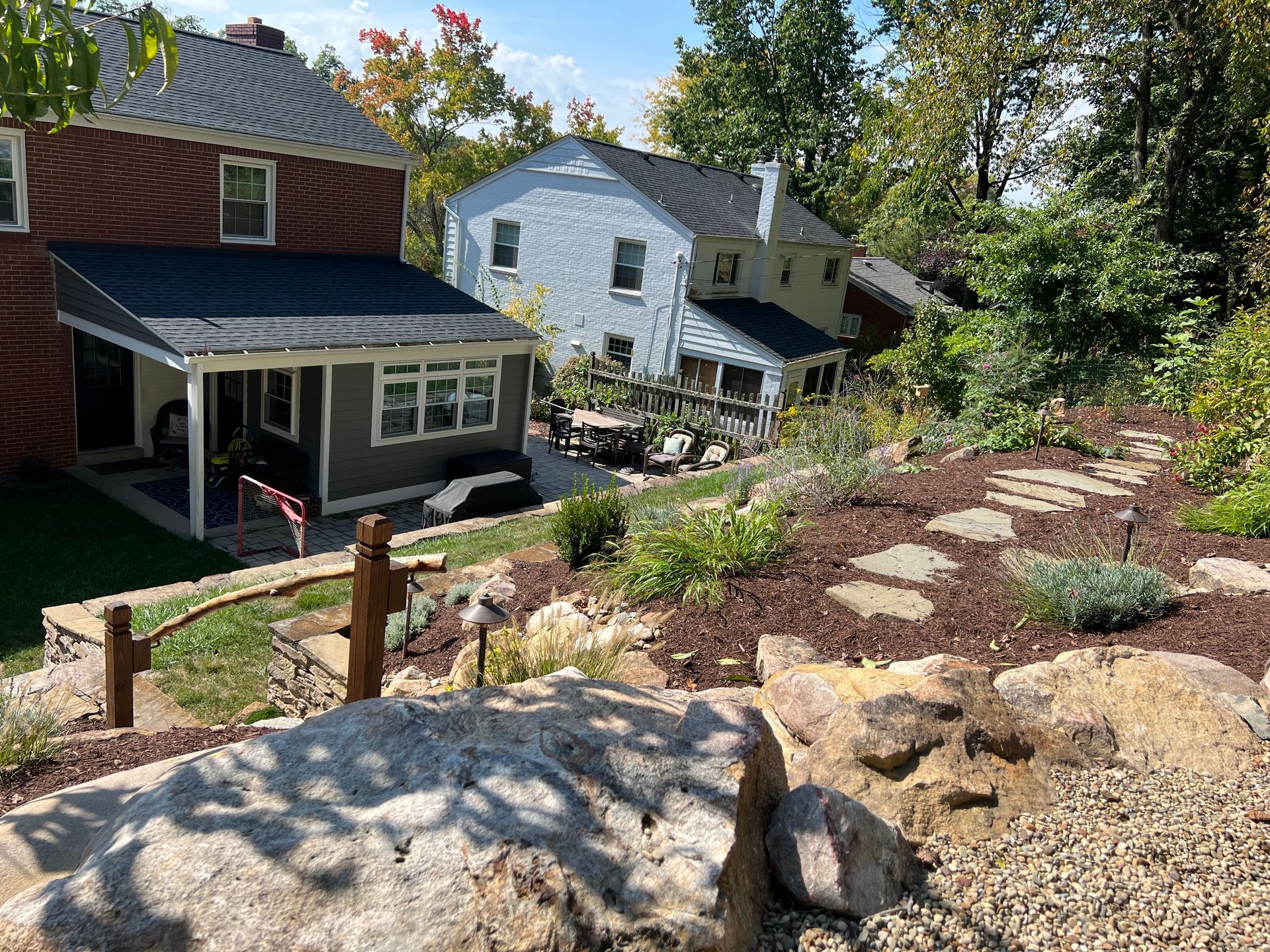 Stone steps through a landscaped backyard toward houses on a sunny hillside