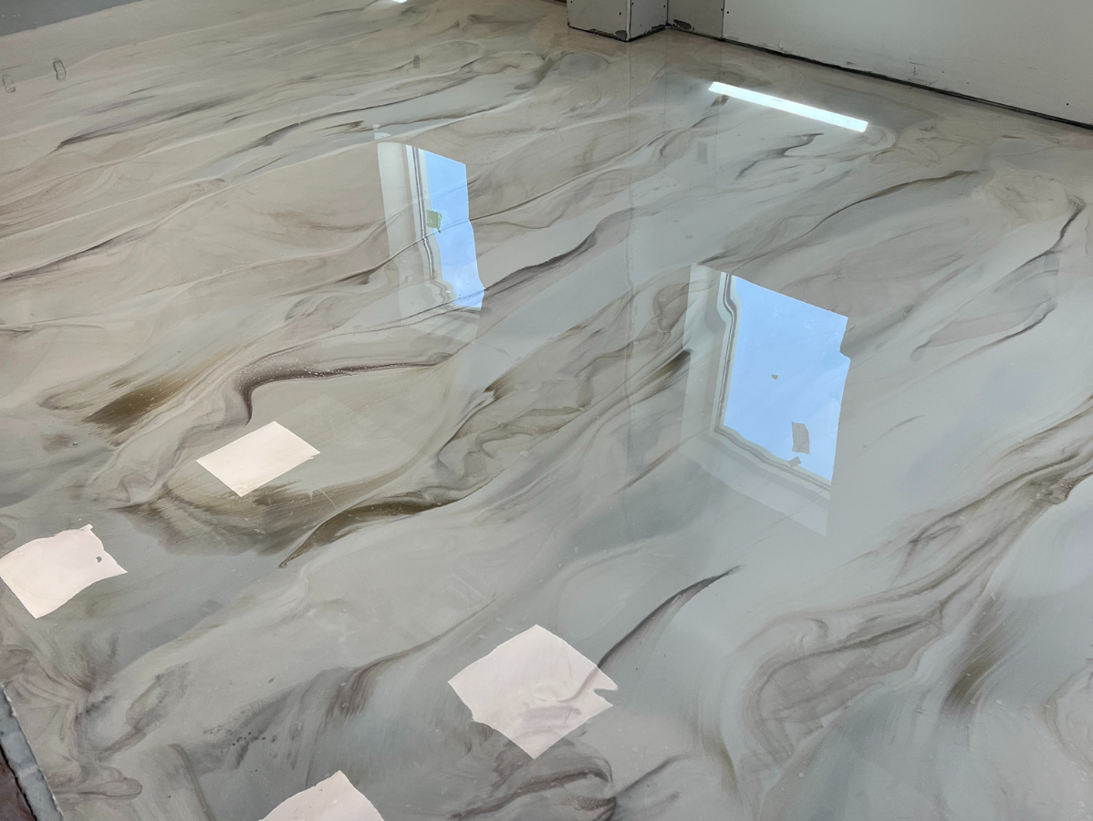Swirling, glossy epoxy floor with white and brown tones, reflecting overhead lights and windows.