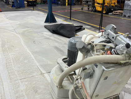 Concrete floor grinding machine in industrial setting, with a work area cordoned off.