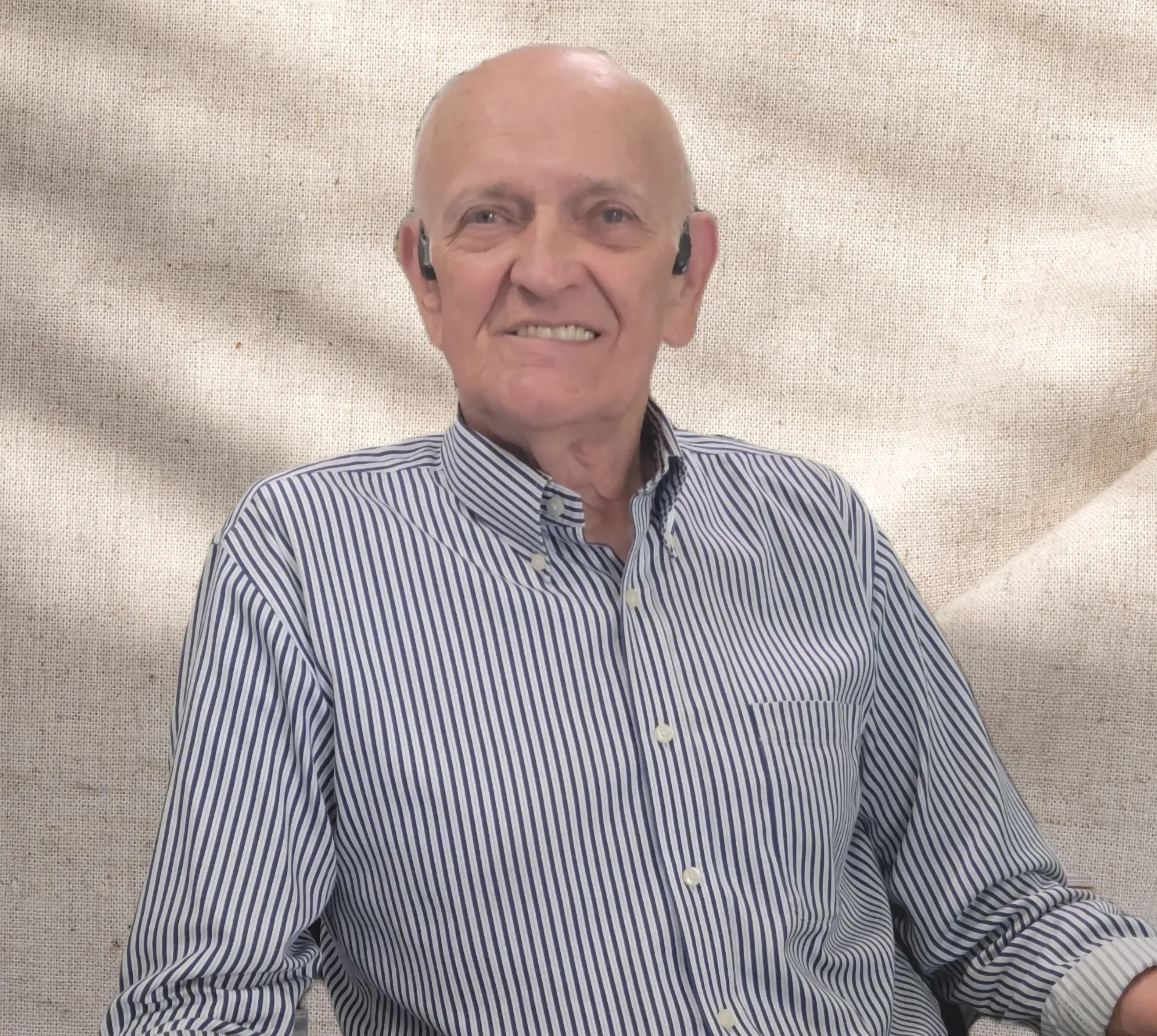 An older man wearing a striped shirt and headphones is sitting on a couch.