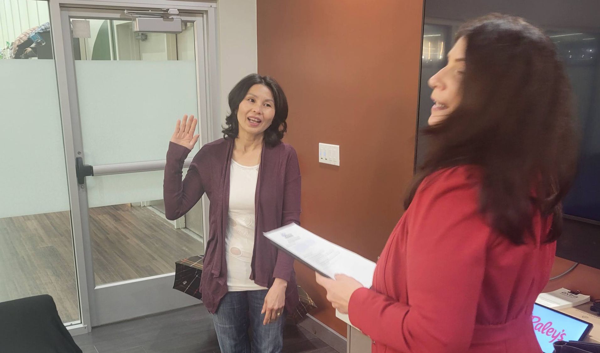 two women are standing next to each other in a room and one is holding a piece of paper .