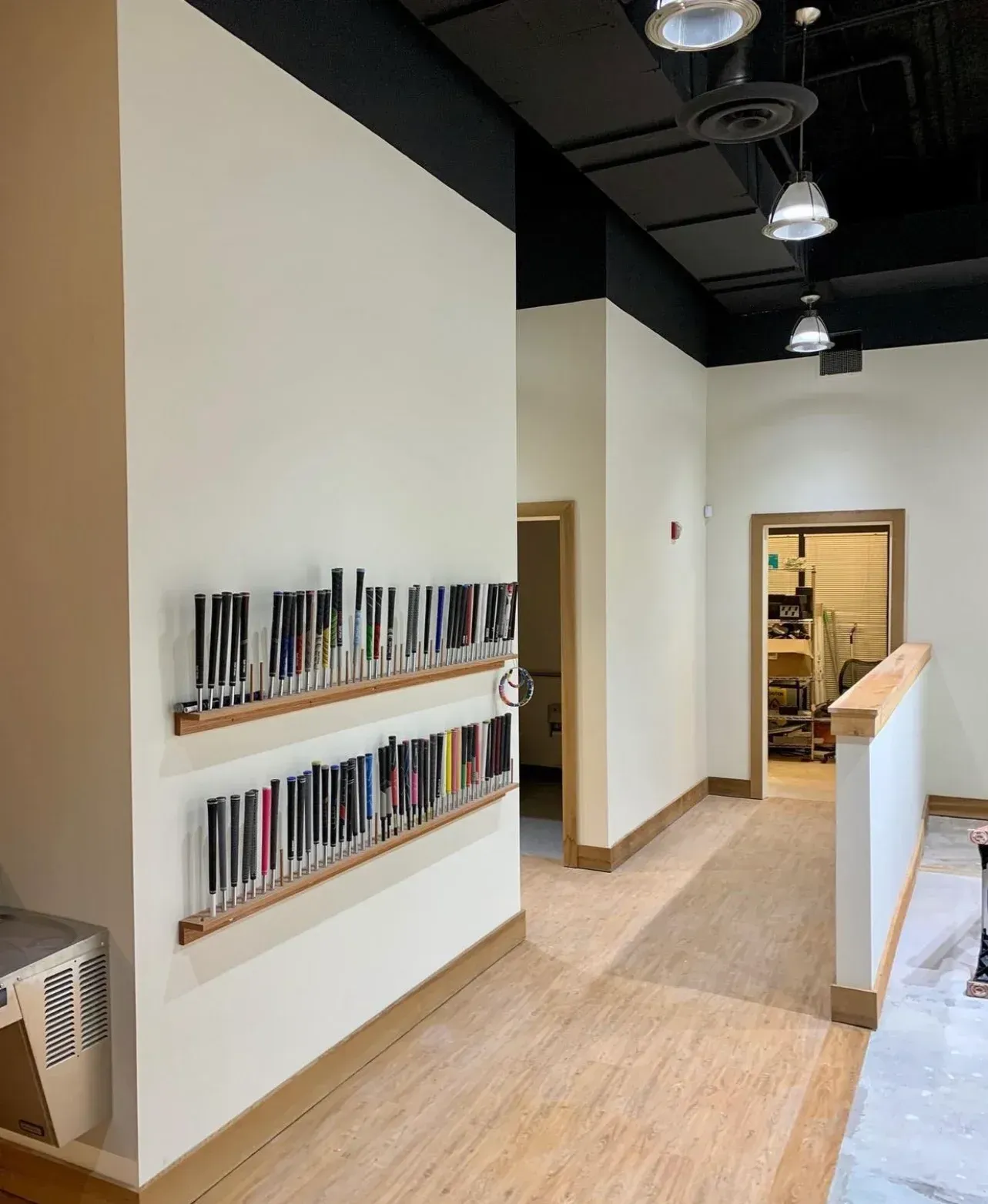 Wall-mounted display racks holding golf club grips on a white wall in an office space with light wood flooring.