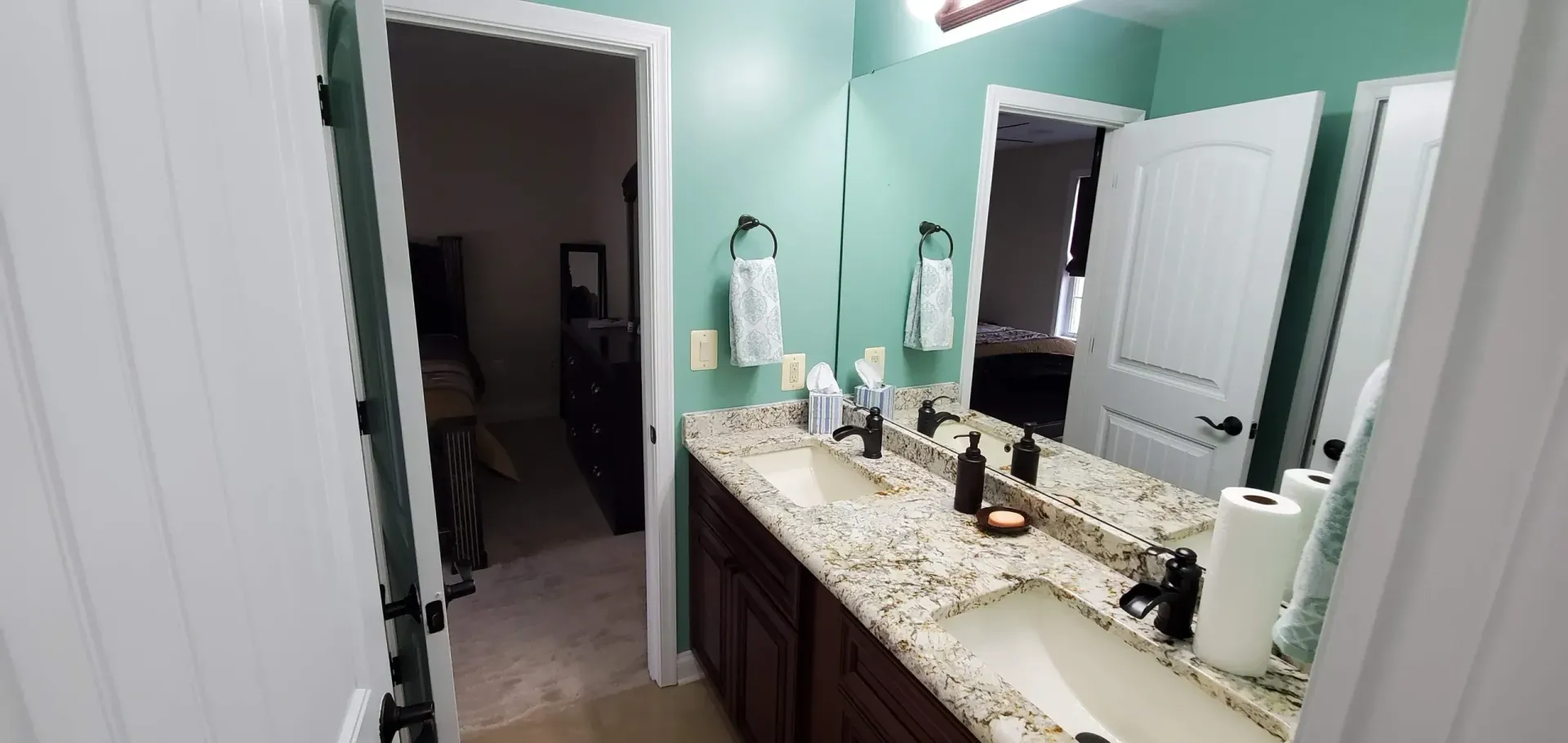 A double-sink bathroom vanity with dark cabinets and granite countertops against a mint green wall.