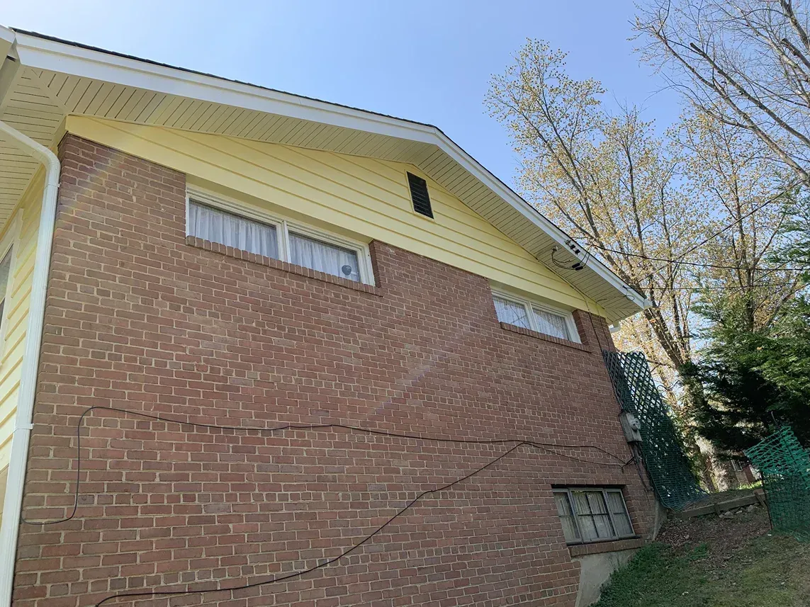 A low-angle view of a brick house exterior with yellow siding, showing a prominent diagonal crack along the brick wall.