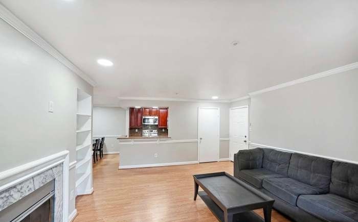 A spacious living room with light walls, hardwood floors, a gray sofa, a dark coffee table, and an open kitchen background.