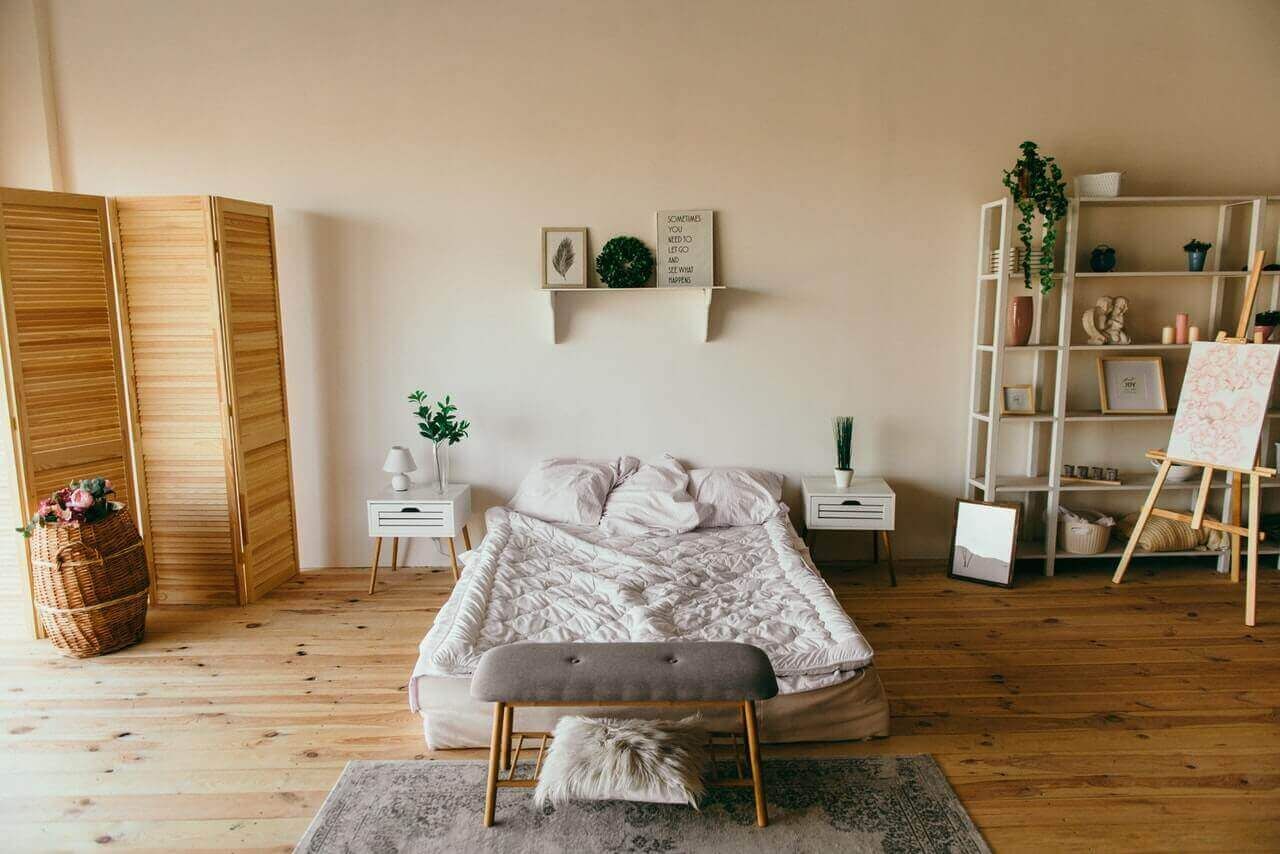 a bedroom with white walls and bedding and light wood flooring