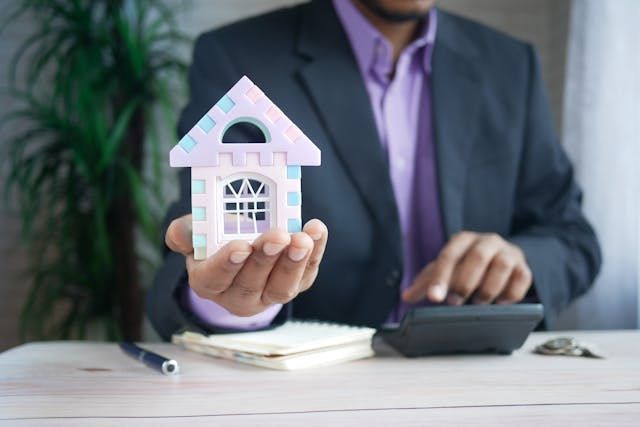 a person holding a home figurine and putting numbers into a calculator