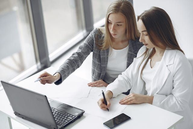 two people sitting at a small desk looking at a computer
