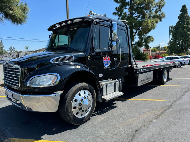 Black tow truck parked in a lot on a sunny day, with a flatbed and chrome front bumper.