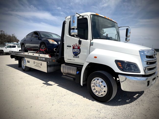 White tow truck hauling a black SUV on a flatbed in a dusty lot
