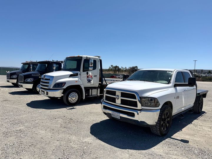 White pickup truck parked on gravel beside several work trucks under a clear blue sky