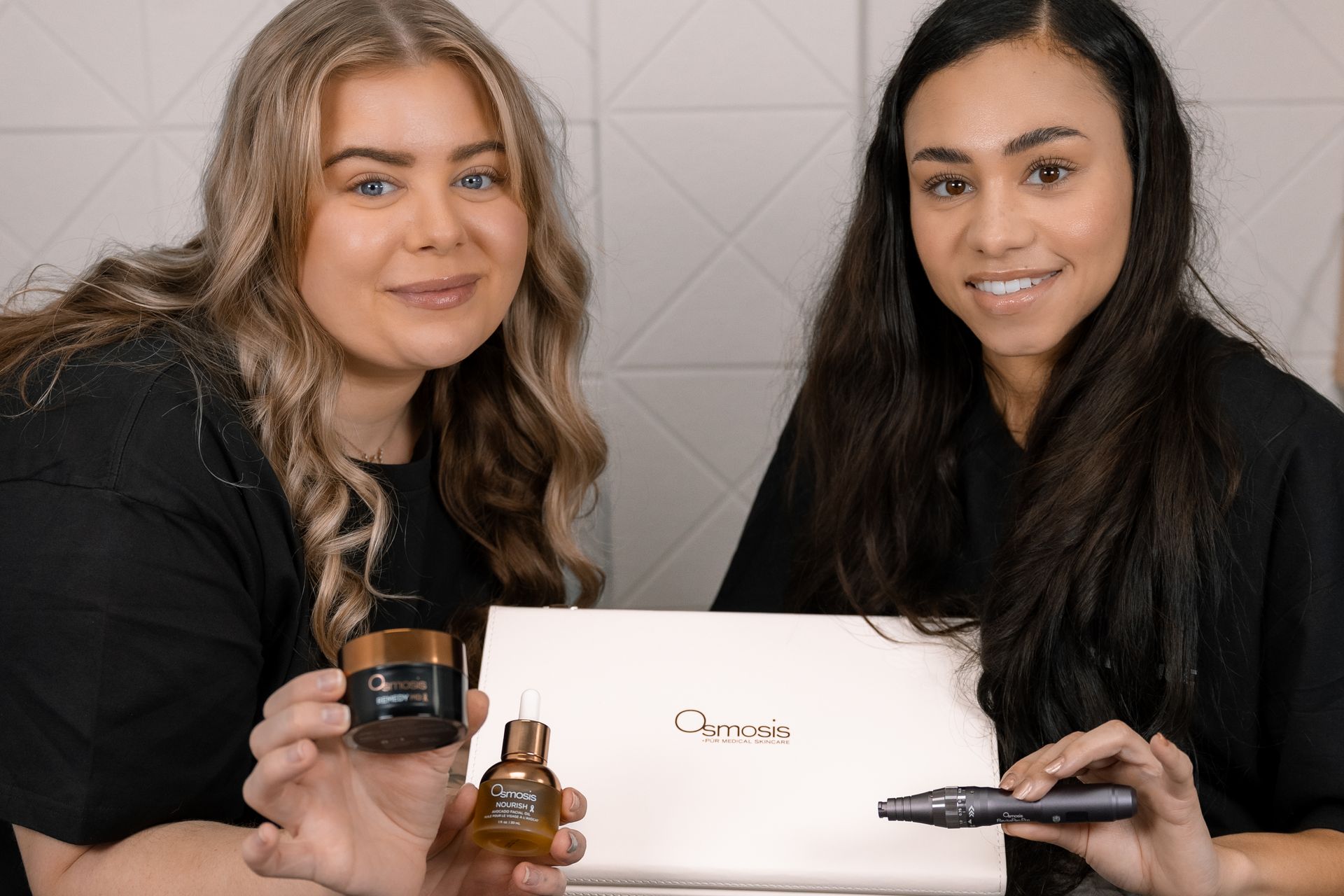 Two women holding beauty products, smiling in front of a white backdrop.