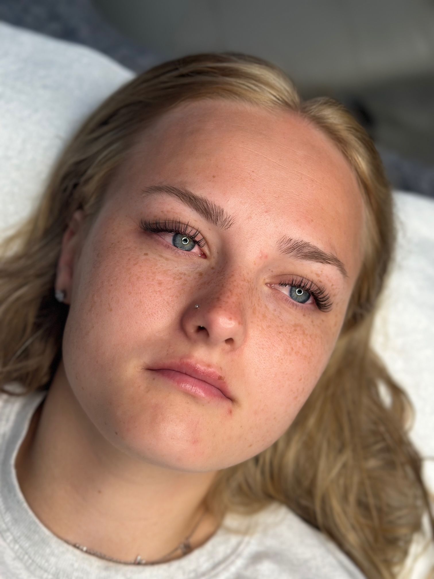 Woman with freckles and dotted eyebrows, looking downward with a neutral expression.