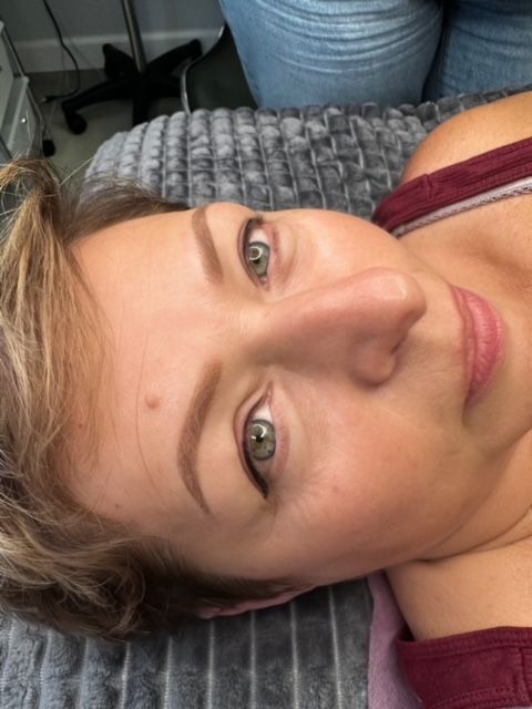 Woman with eyeliner and eyebrow makeup lies on a bed. Close-up of face.