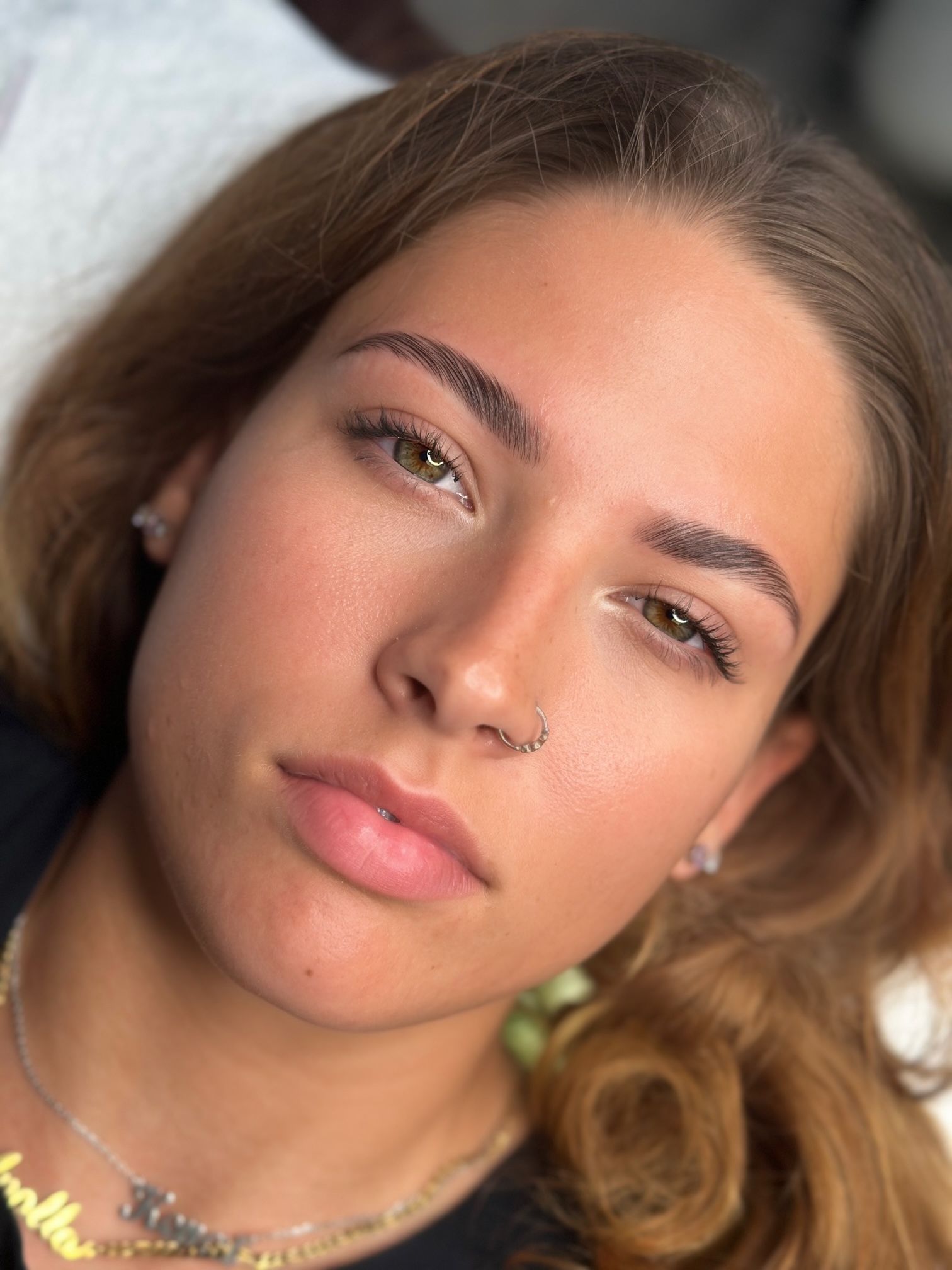 Woman with newly tattooed eyebrows; close-up, focused face, subtle expression, lying down.