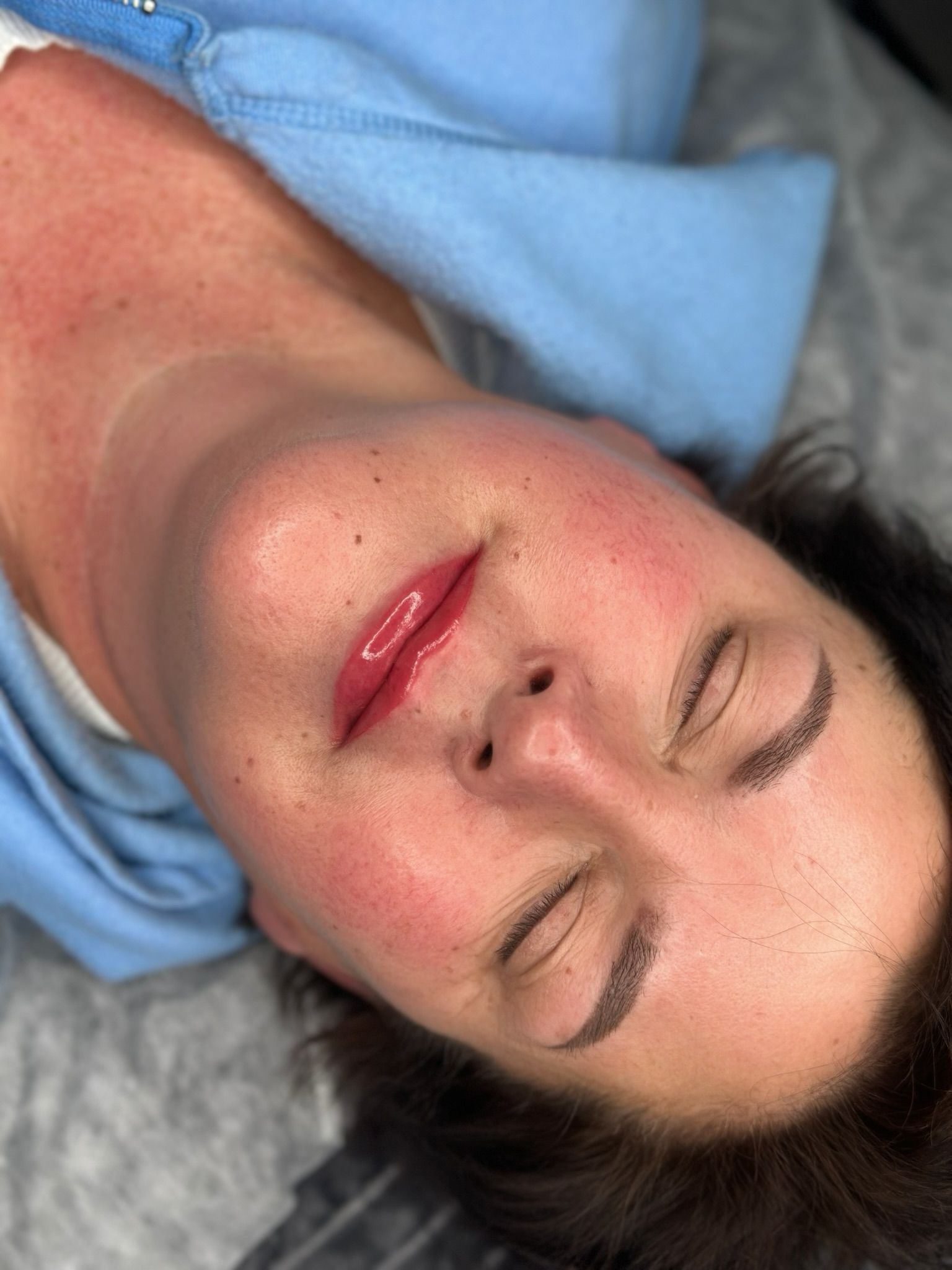 Woman with closed eyes, lip tint, freckles, and eyebrow tattoo, possibly after a cosmetic procedure.