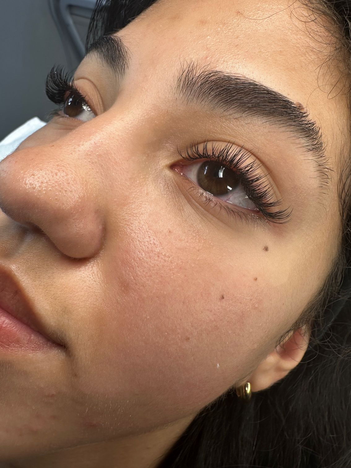 Close-up of a person's face; brown eyes, eyebrows, and lashes covered with black dots. Skin is lightly colored.