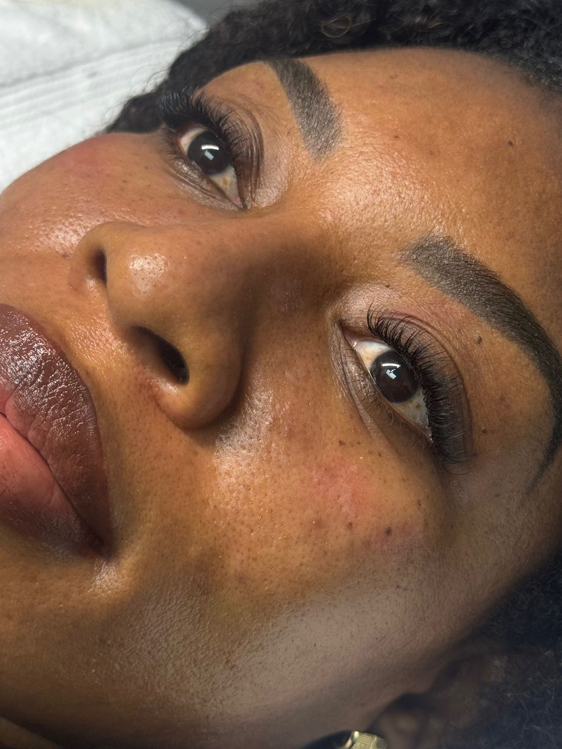 Close-up of a person's face with makeup. Their skin is smooth with defined eyebrows and dark eyes.