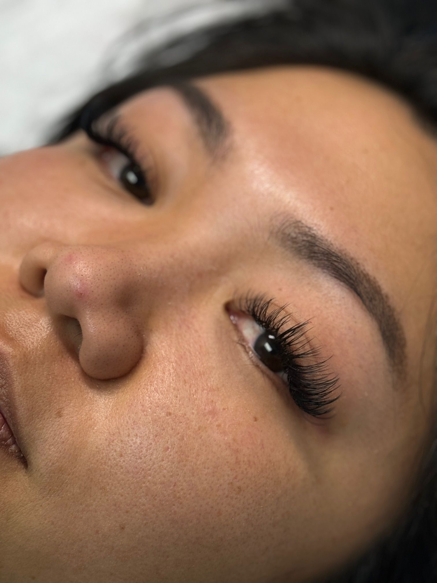 Close-up of a person's eye with prominent eyelashes and a subtly arched eyebrow. Skin is visible, with a light complexion.