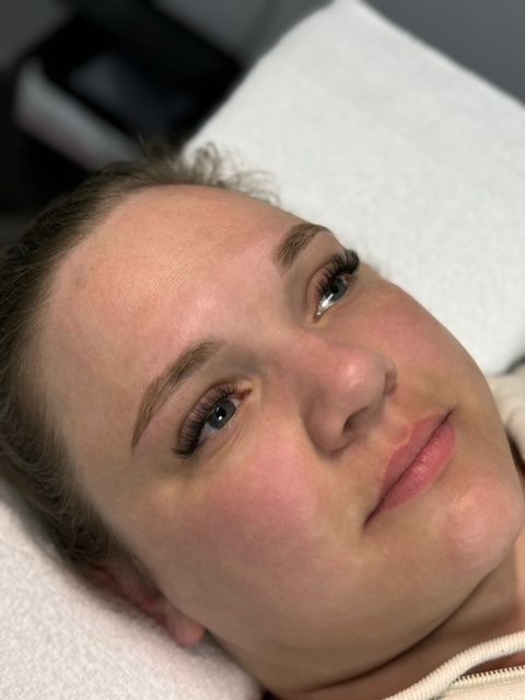 Woman with filled-in eyebrows and eyelashes, lying down. Soft lighting, subtle makeup.