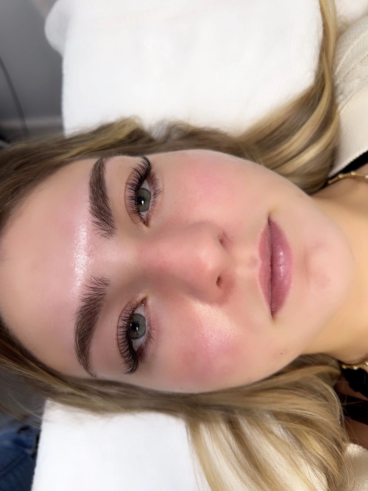 Woman with newly tattooed eyebrows and lips. Lying on a white surface, with blonde hair.