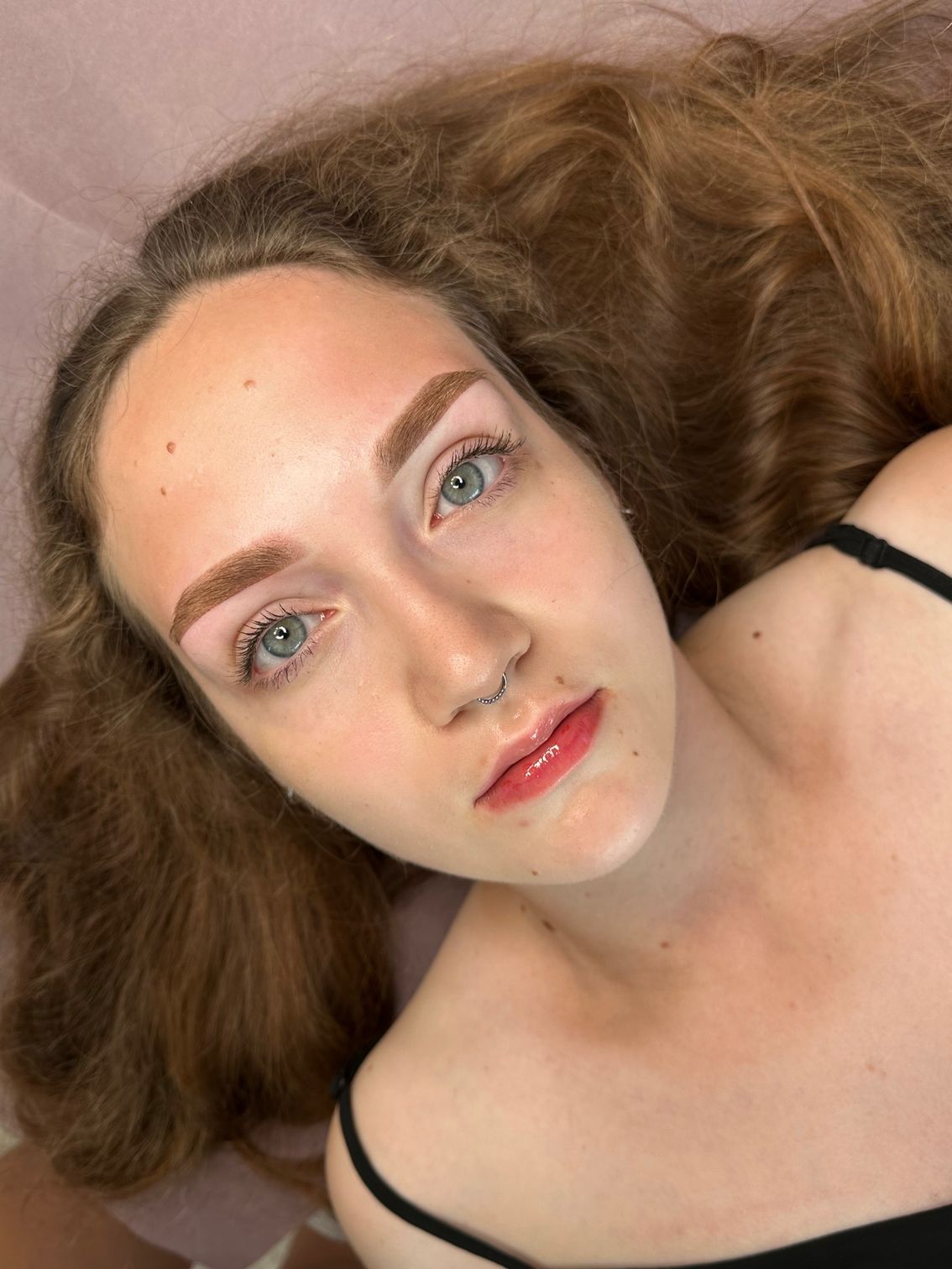Woman with red-brown hair and new eyebrow microblading, looking at the camera.