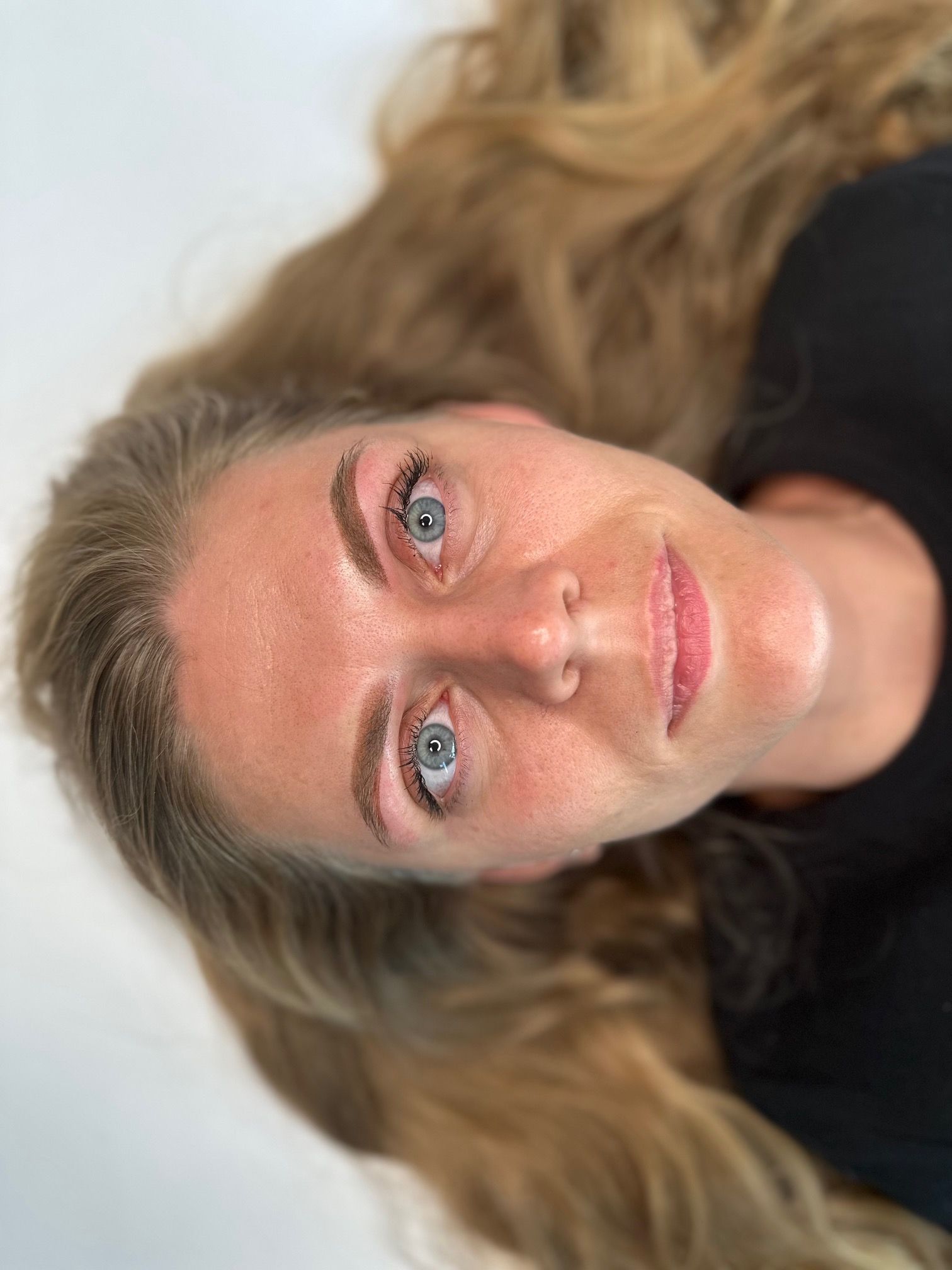 Woman with blonde hair, freckled face, and newly tattooed eyebrows, looking up.