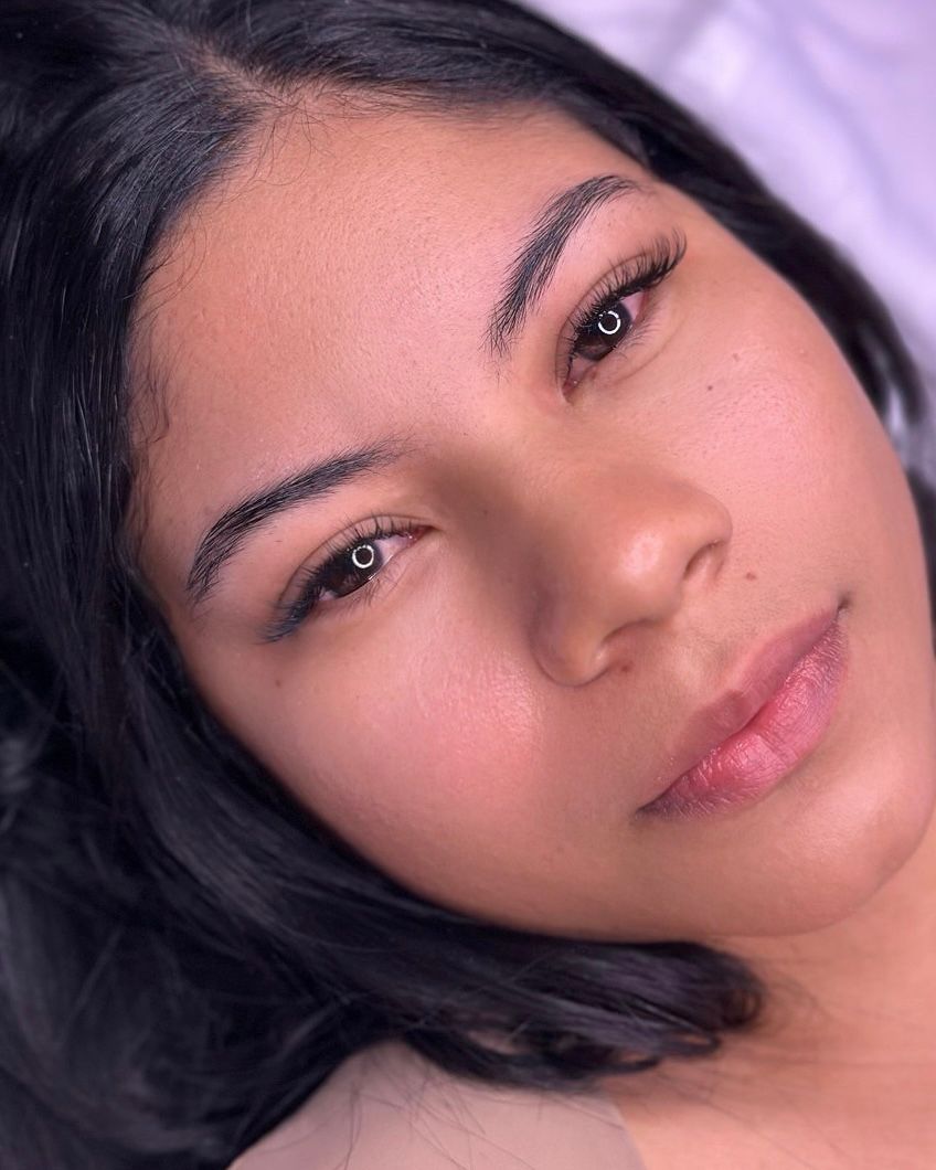 Woman with freshly microbladed eyebrows; close-up shows dark ink and slight redness on skin.