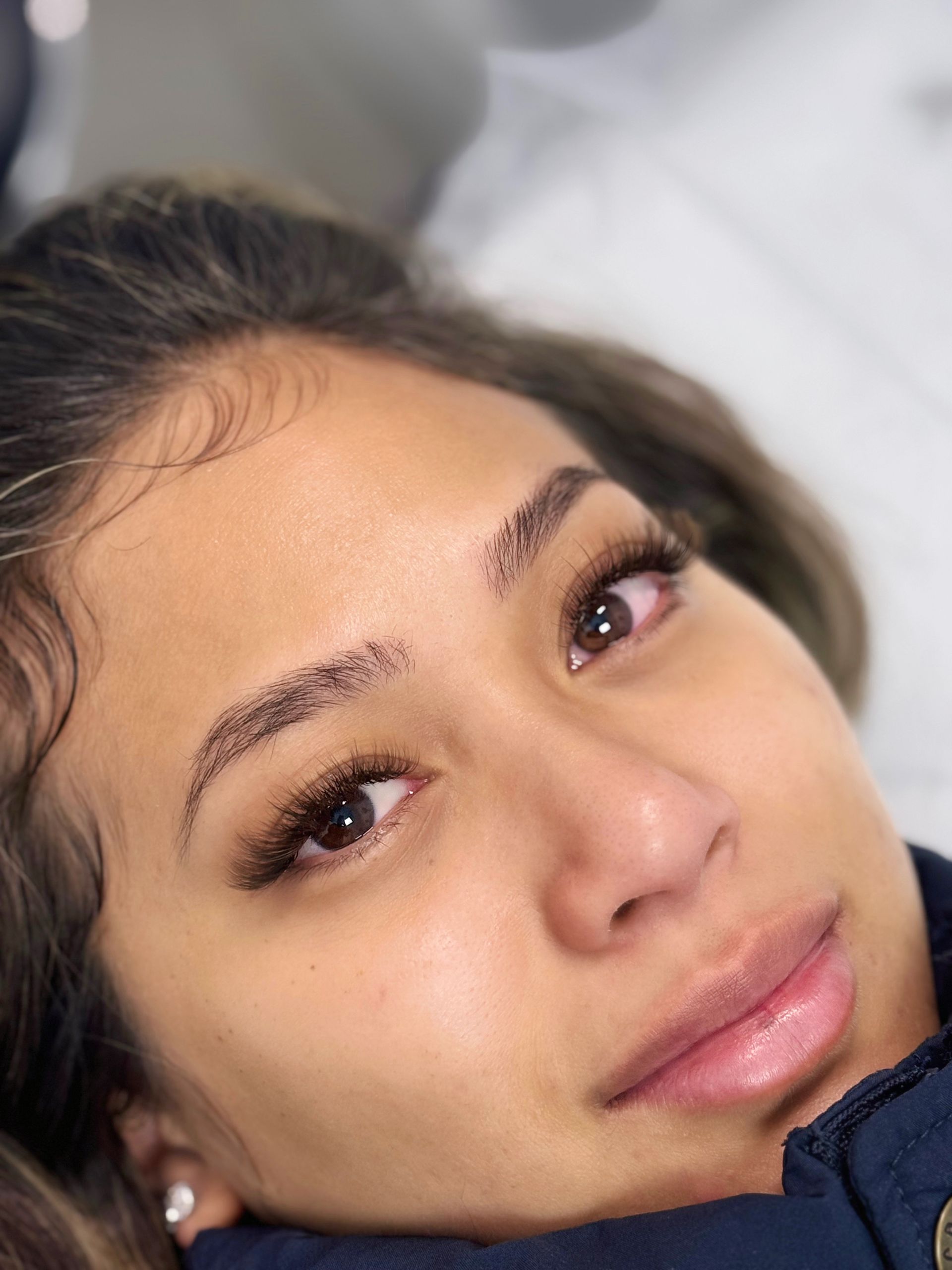 Woman with tattooed eyebrows and eyelash extensions looking towards the viewer.