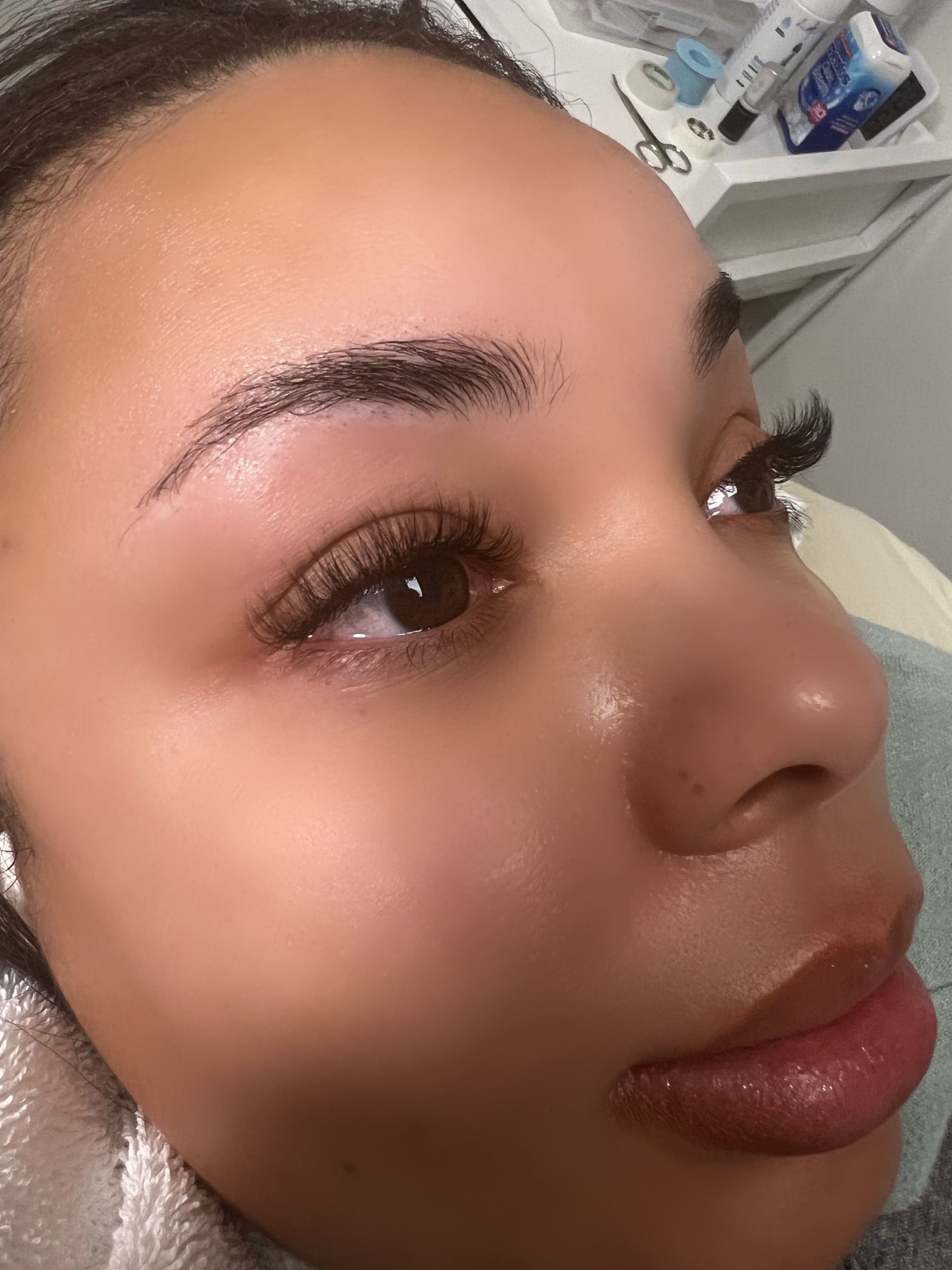 Close-up of person's face; eyebrow tattoo process in progress, with enhanced lashes and plump lips.