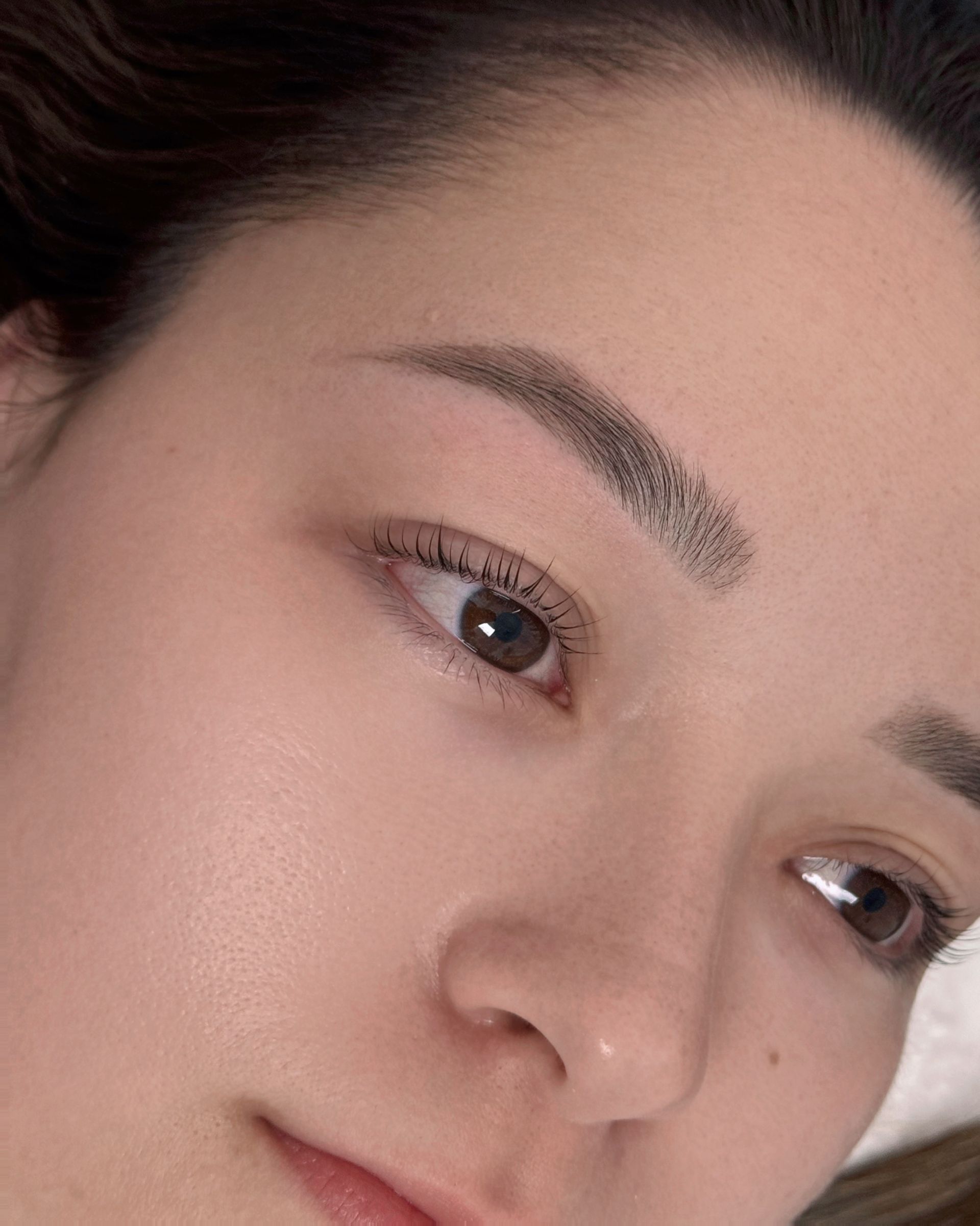 Woman's face close-up, with eyebrow and eyeliner microblading. Light skin, brown eyes, soft focus.