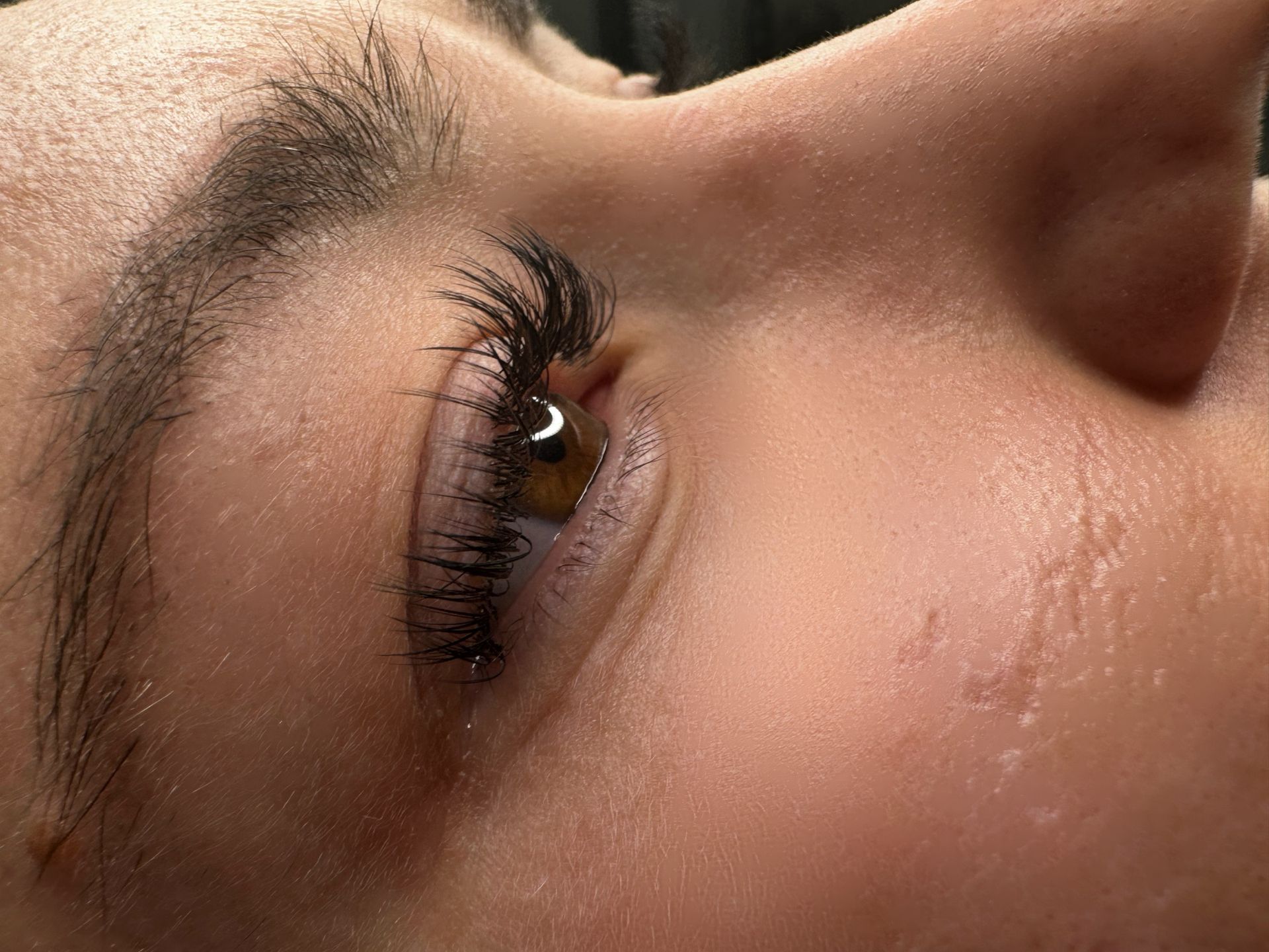 Close-up of an eye with thick, dark lashes. A brown iris is visible. The skin is pale.