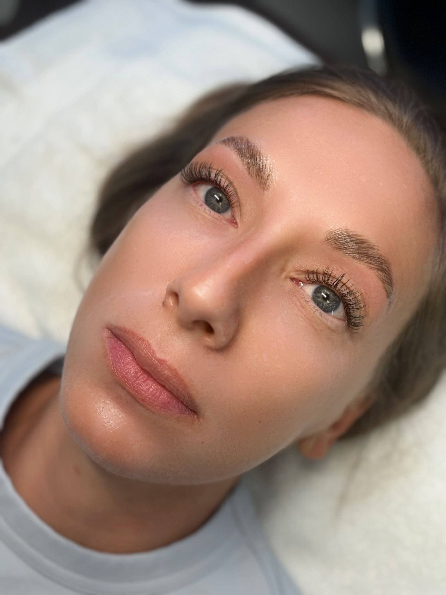 Woman with freshly tattooed eyebrows, lying on a white bed.