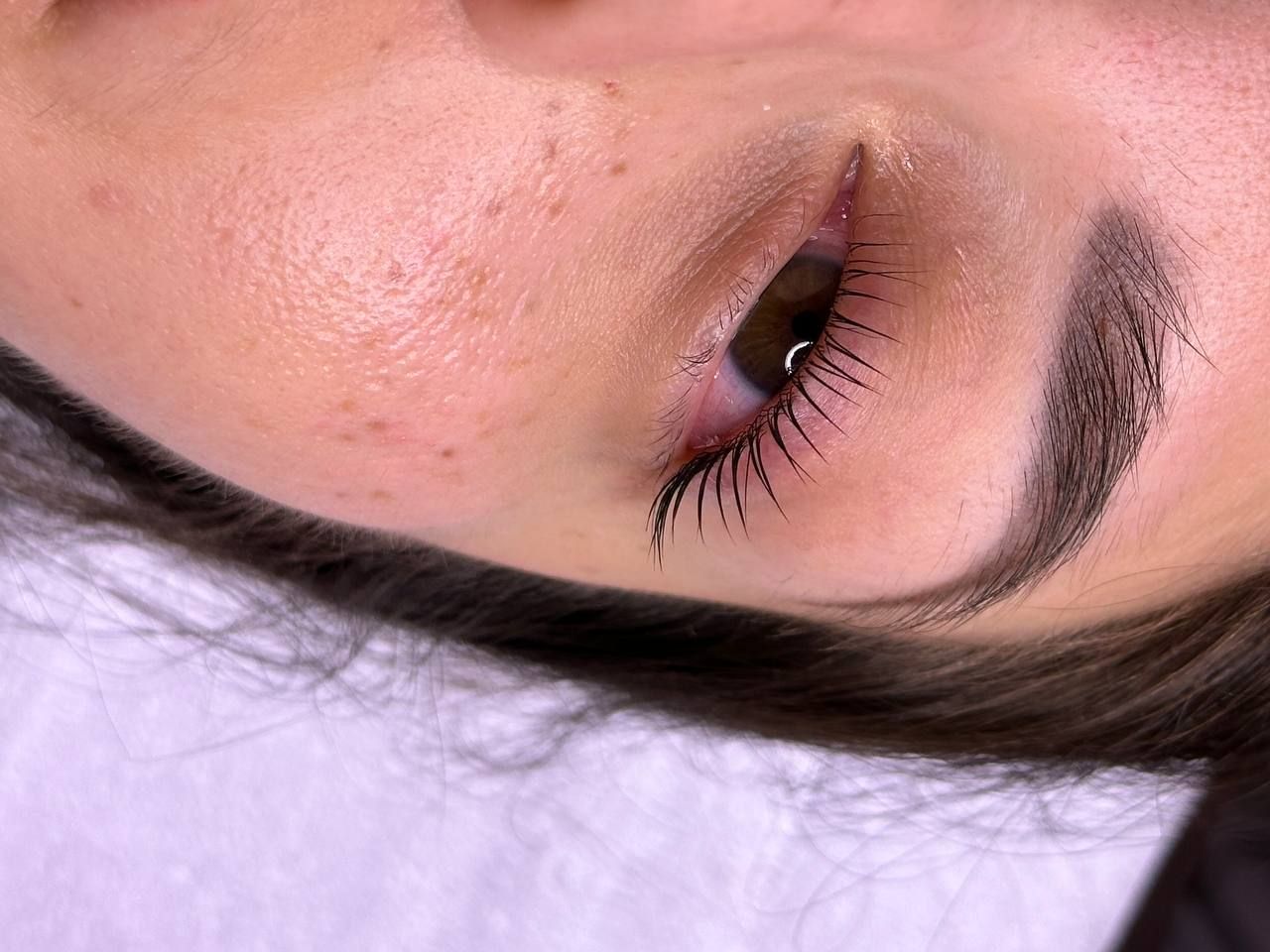 Close-up of a person's eye, showing a tattooed eyeliner and sparse lashes; skin is slightly pink.