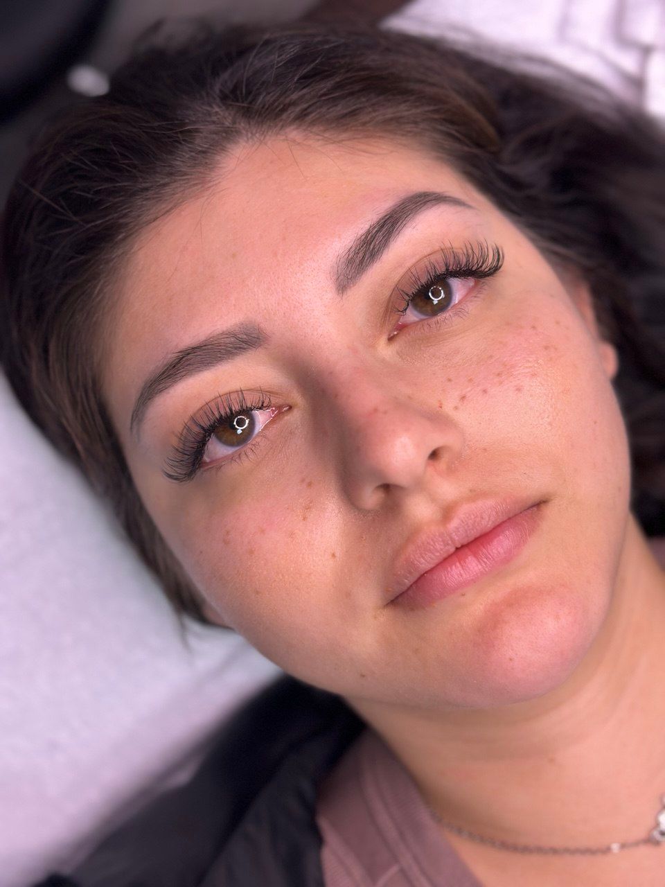 Woman with semi-permanent makeup: microbladed eyebrows and eyelash extensions, resting face, freckled skin.