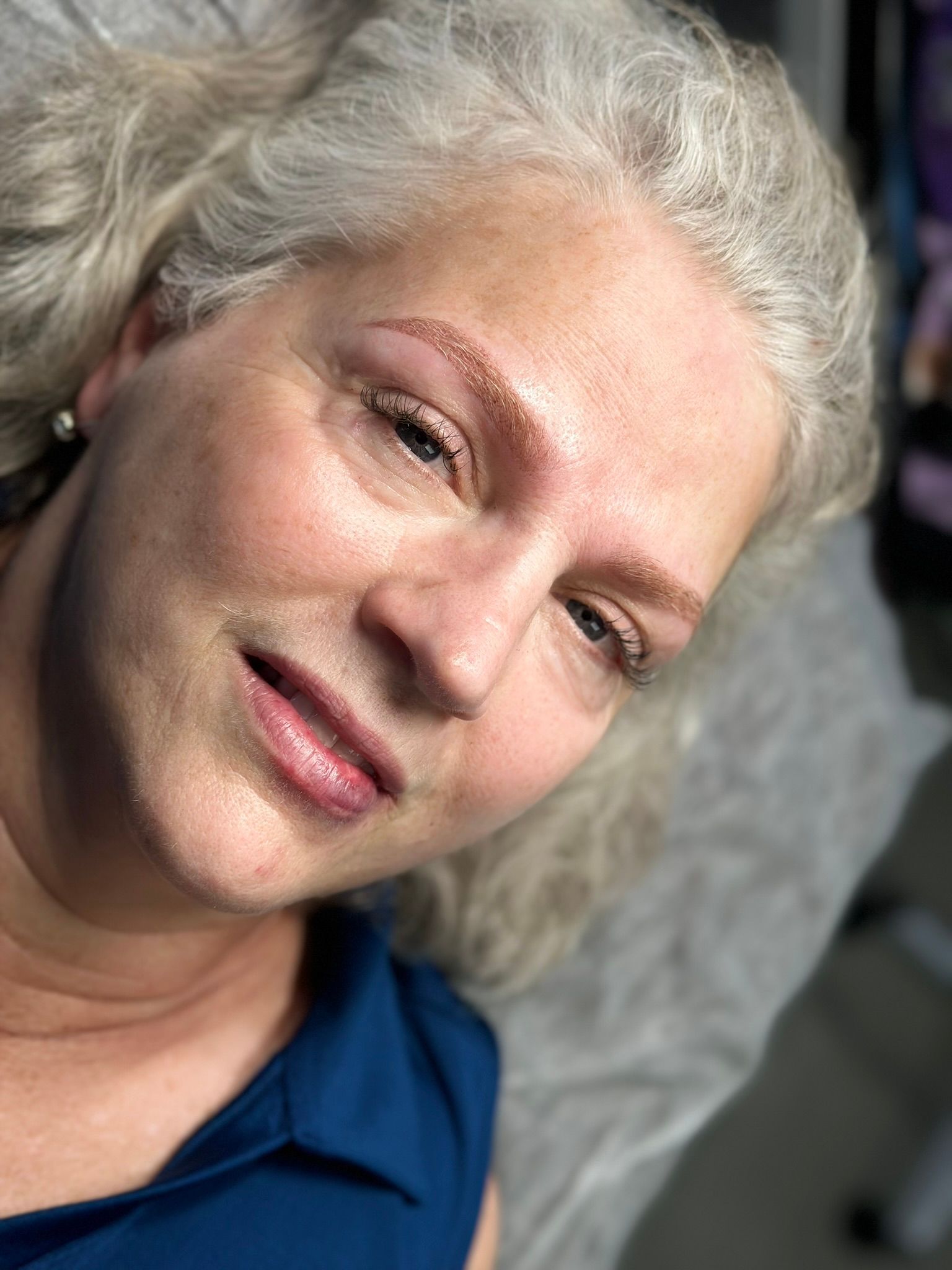 Woman with light eyebrows, fresh microblading, and light skin, on a white surface.