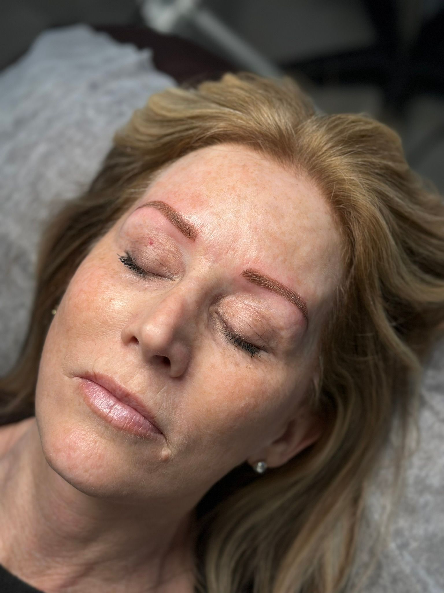 Woman with closed eyes, after eyebrow microblading procedure.