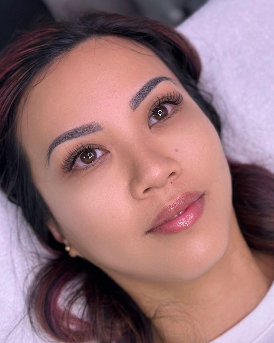 Woman with styled eyebrows and eyelashes, wearing light makeup, looking upwards.