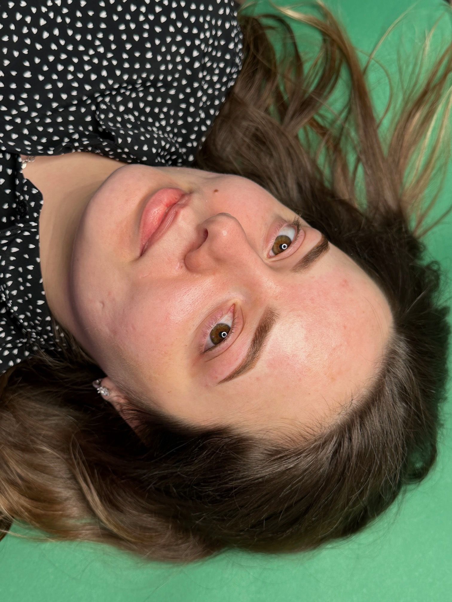 Woman with microbladed eyebrows, lying down with green surface beneath.