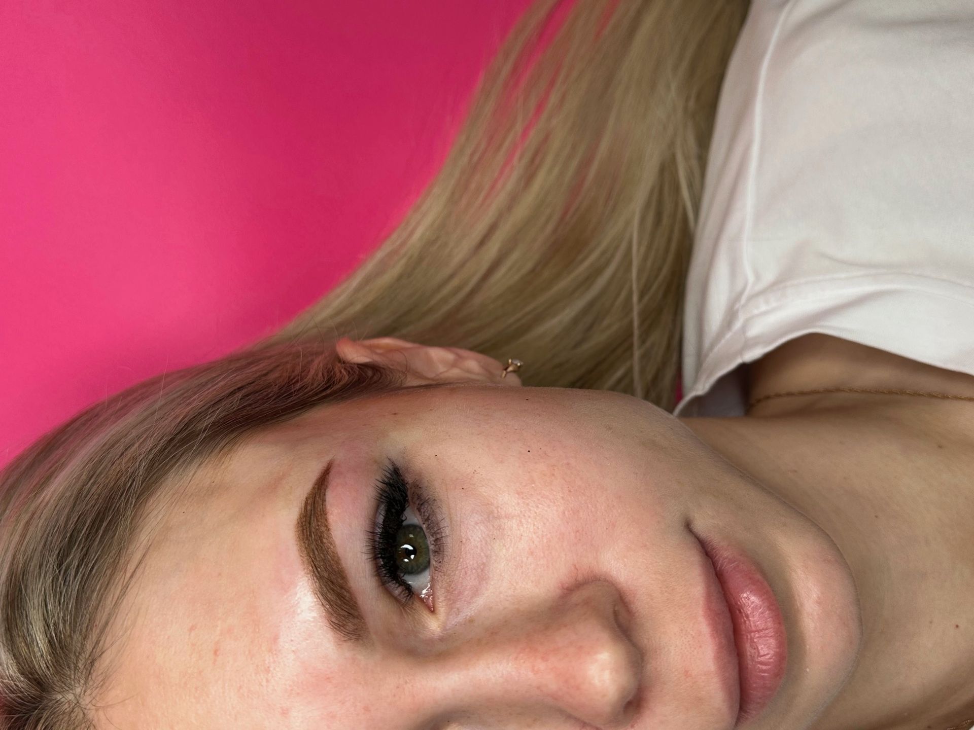 Woman with blonde hair and dark eyebrows, eye makeup, and pink lipstick, against a pink background.