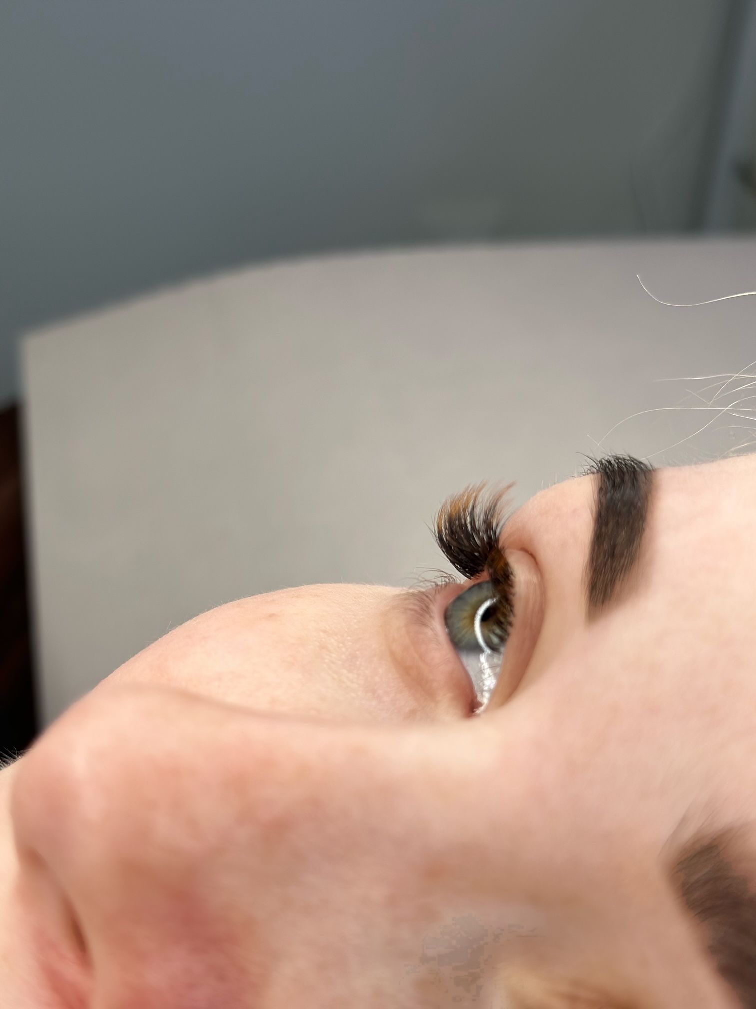 Close-up of a person's eye with eyebrow makeup and eyelash extensions, lying down, looking up.