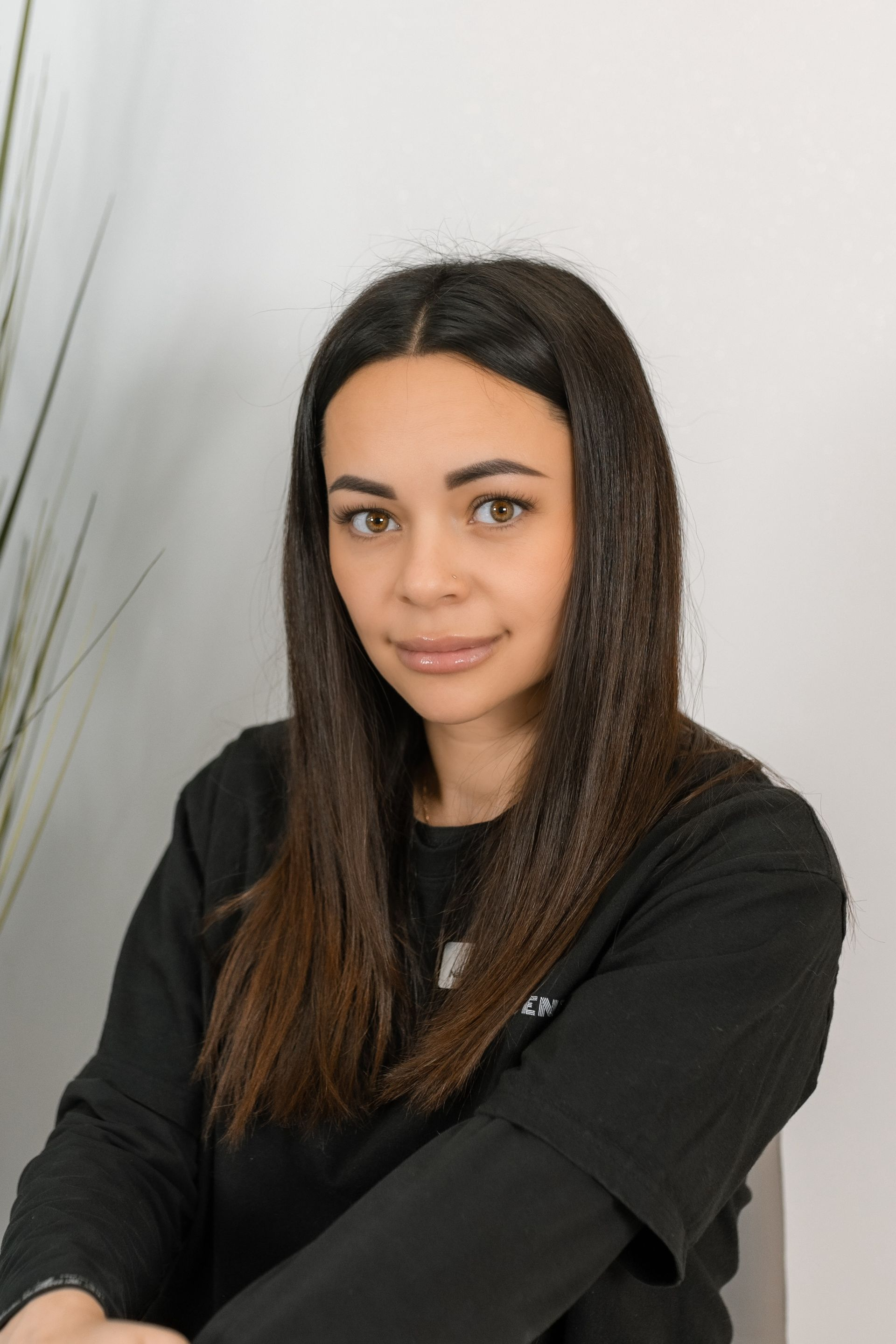 Woman with long brown hair, wearing a black shirt, looking at the camera. Neutral background.