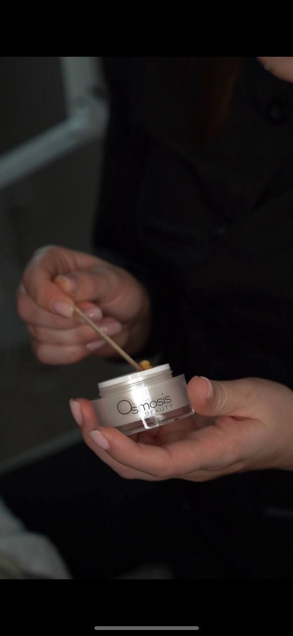 Person holding a jar of cream and a wooden stick, seemingly applying the cream.