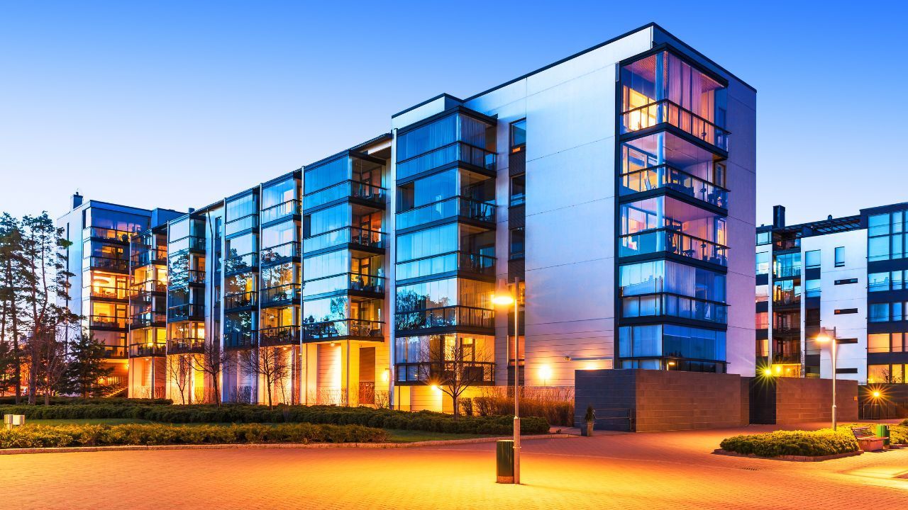 Modern glass apartment building glowing at dusk with warm interior lights and a lit walkway