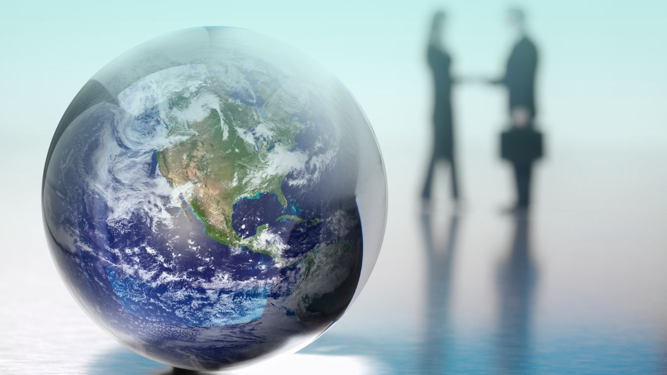 A handshake between professionals in front of a globe, representing international tax compliance for manufacturing businesses.