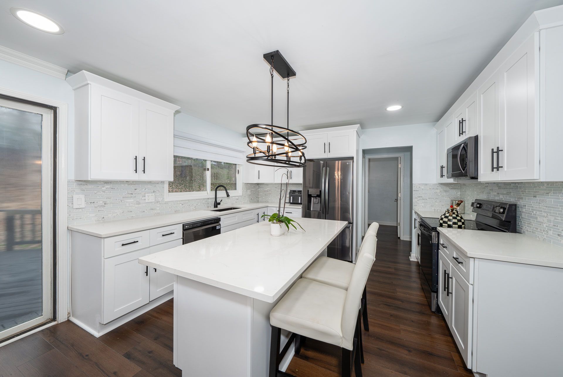 Bright modern kitchen with white cabinets, island, stools, and stainless steel appliances.