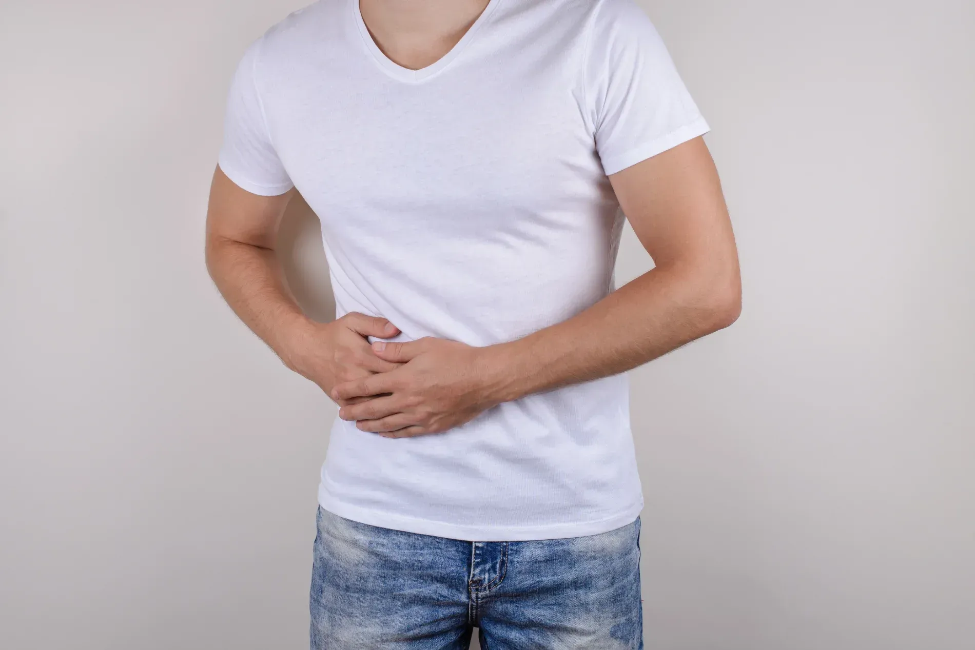 Man in white shirt and jeans holds his stomach, possibly in pain  — Tewantin Medical Centre In Tewantin, QLD