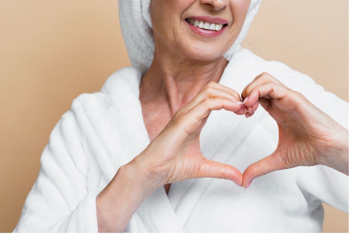 Woman in white robe and towel making a heart shape with her hands, smiling  — Tewantin Medical Centre In Tewantin, QLD
