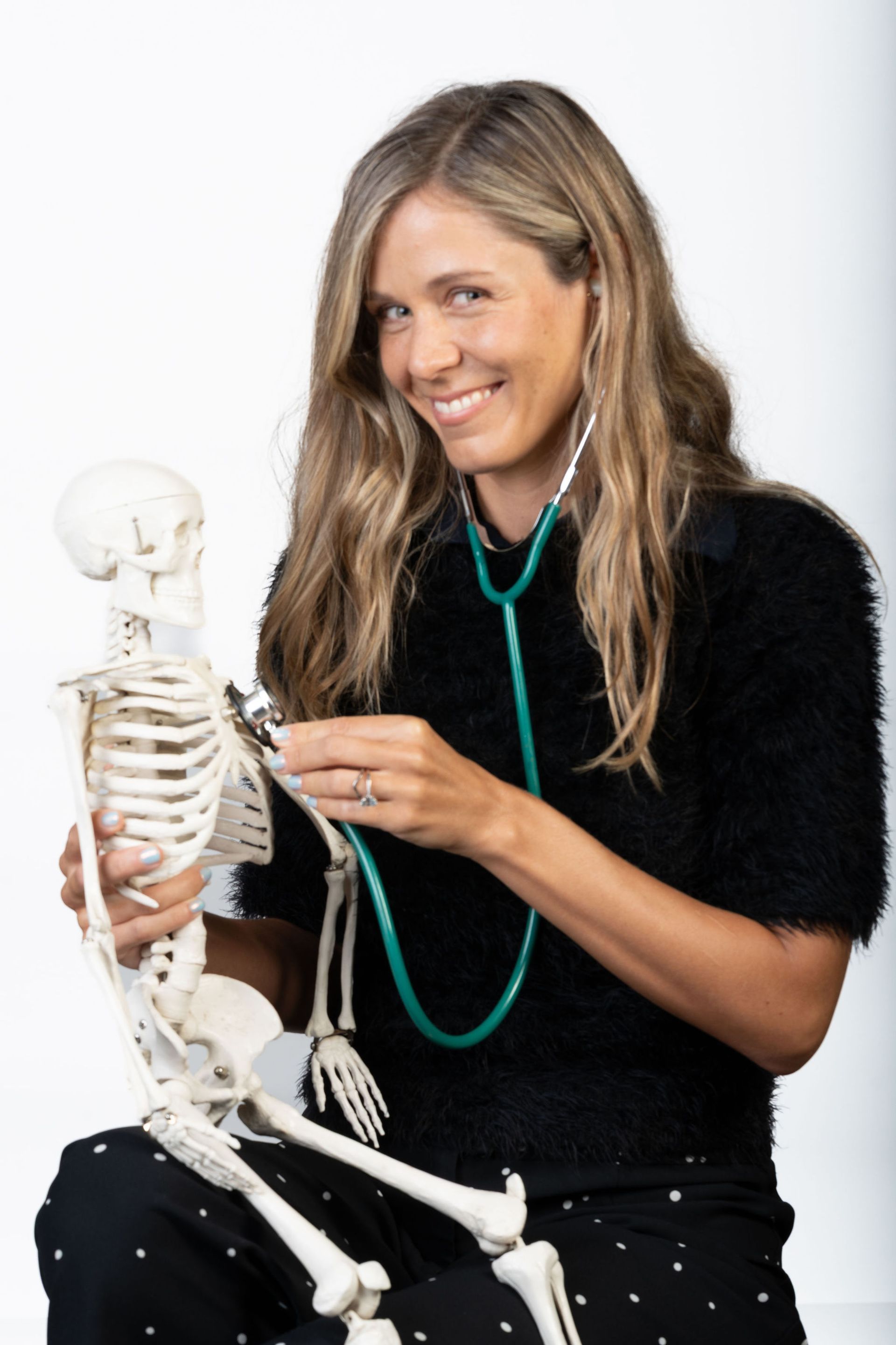Woman with stethoscope examining a skeleton, smiling; white background  — Tewantin Medical Centre In Tewantin, QLD