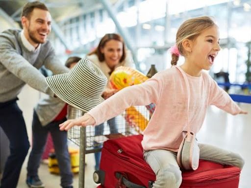 Family at Airport, Girl Laughing on Luggage, Arm Outstretched, Parent Pushing Cart — Tewantin Medical Centre In Tewantin, QLD